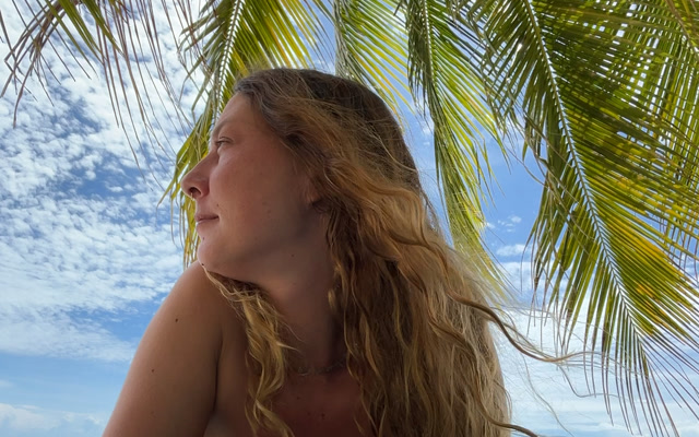Sarah under a palm tree looking out at the sea